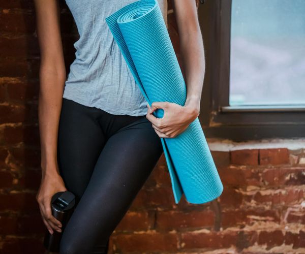 A neatly rolled yoga mat next to a small plant and a water bottle.